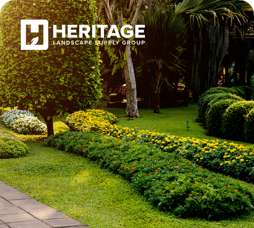 A lush garden featuring colorful flowers and neatly trimmed hedges, with a logo for Heritage Landscape Supply Group in the corner.