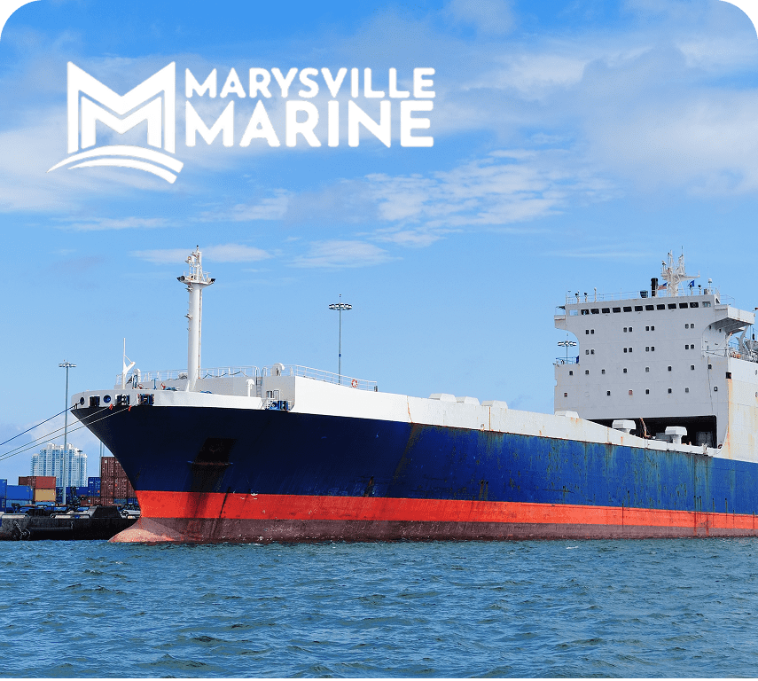 Cargo ship docked at port against a blue sky, featuring the Marysville Marine logo above.